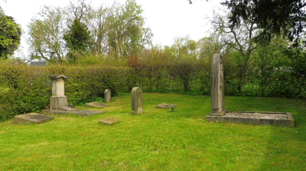 Das Bild zeigt das Gräberfeld der Zwangsarbeiter*innen am Friedhof Ihringshausen. Wenige, teils zerstörte, Grabsteine und -platten sind zu sehen, umringt wird das Feld von einer Hecke.